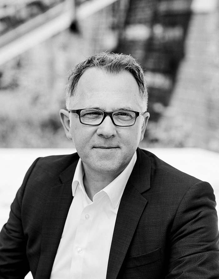 Ein Mann mittleren Alters mit Brille blickt neutral in die Kamera, draußen aufgenommen; Kanzlei Rechtsanwalt Unterföhring.