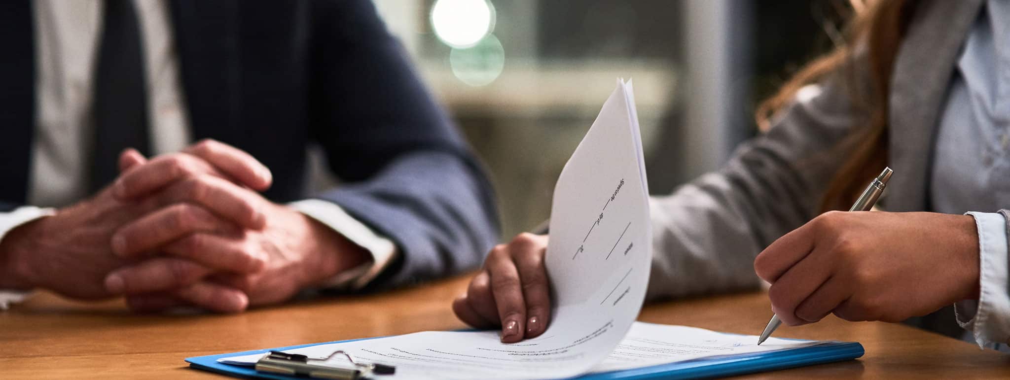 Zwei Personen unterzeichnen Dokumente an einem Holztisch im Büro der Lkm GmbH Rechtsanwälte & Steuerberater in München.