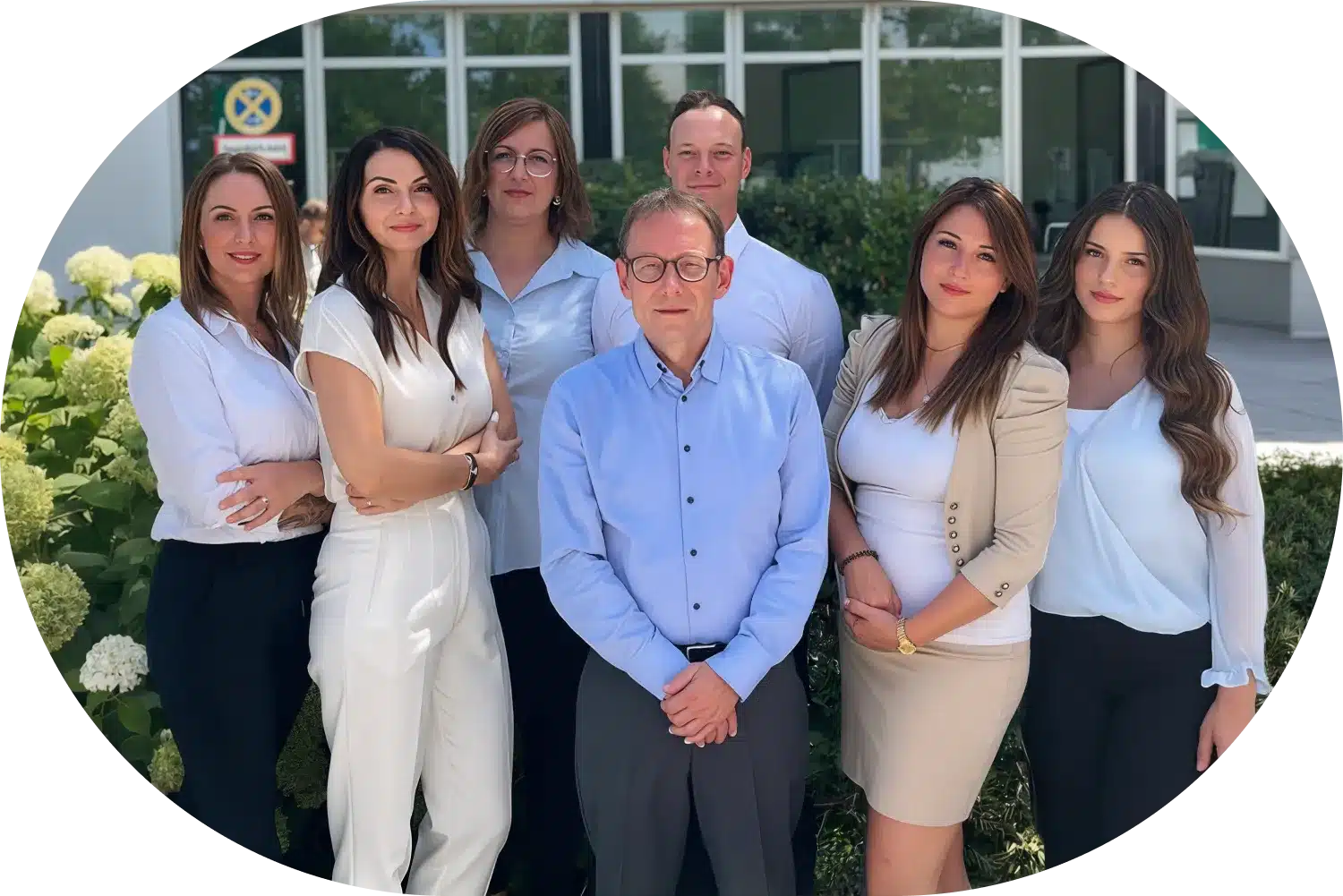 Team der Lkm GmbH steht in Businesskleidung vor Glasfassade mit Pflanzen; Experten für Steuerberatung und Rechtsberatung.