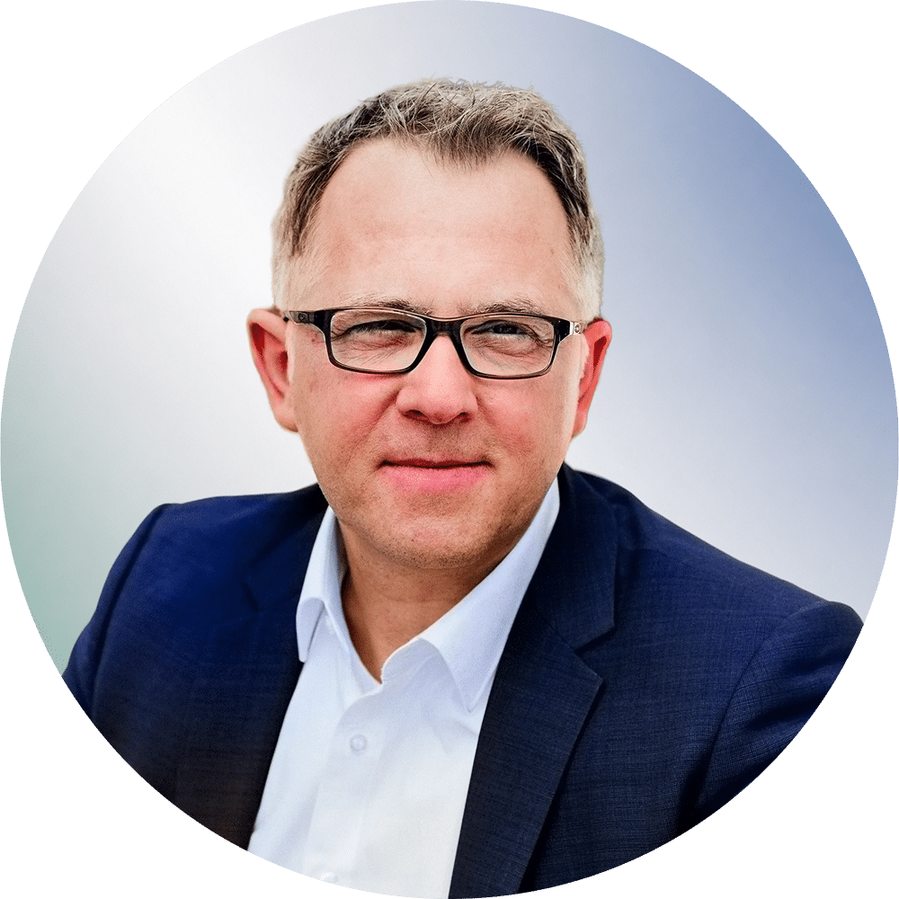 Ein Mann mit Brille und dunklem Sakko blickt ernst in die Kamera, heller Hintergrund. Anwaltskanzlei in Unterföhring.