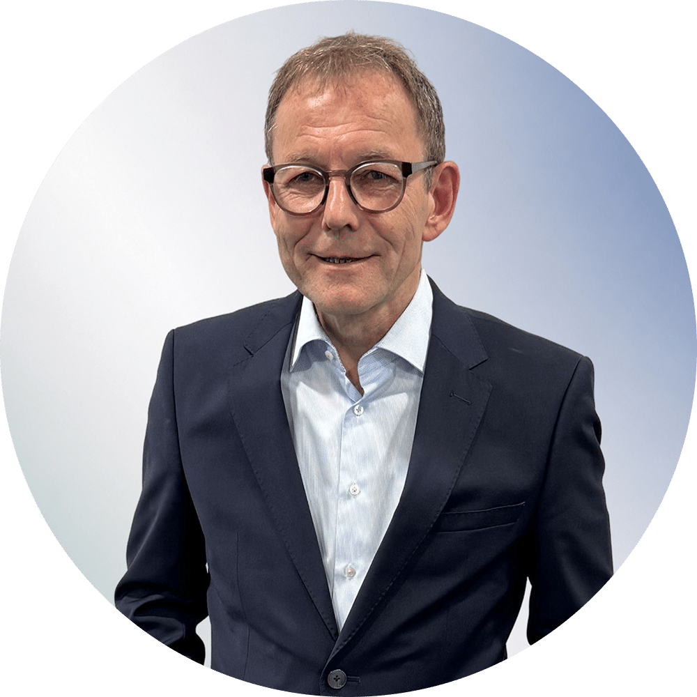 Mann mit Brille in einem dunklen Anzug und einem hellblauen Hemd vor einem hellen Farbverlauf, freundlich, für die Anwaltskanzlei in Unterföhring.