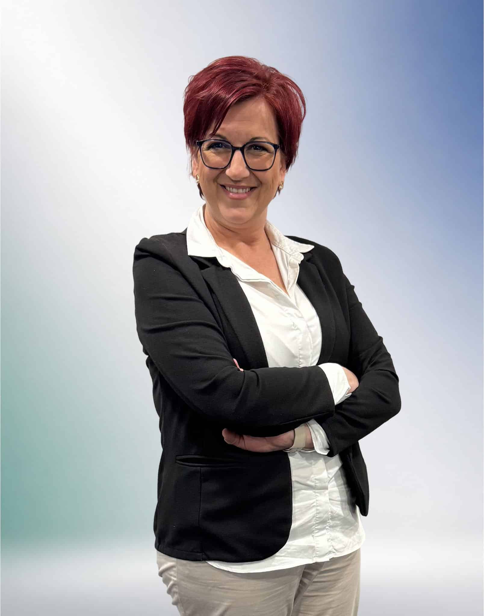 Eine selbstbewusste Person mit roten Haaren und Brille lächelt in Business-Kleidung für das Steuerberater-Profil in Unterföhring.