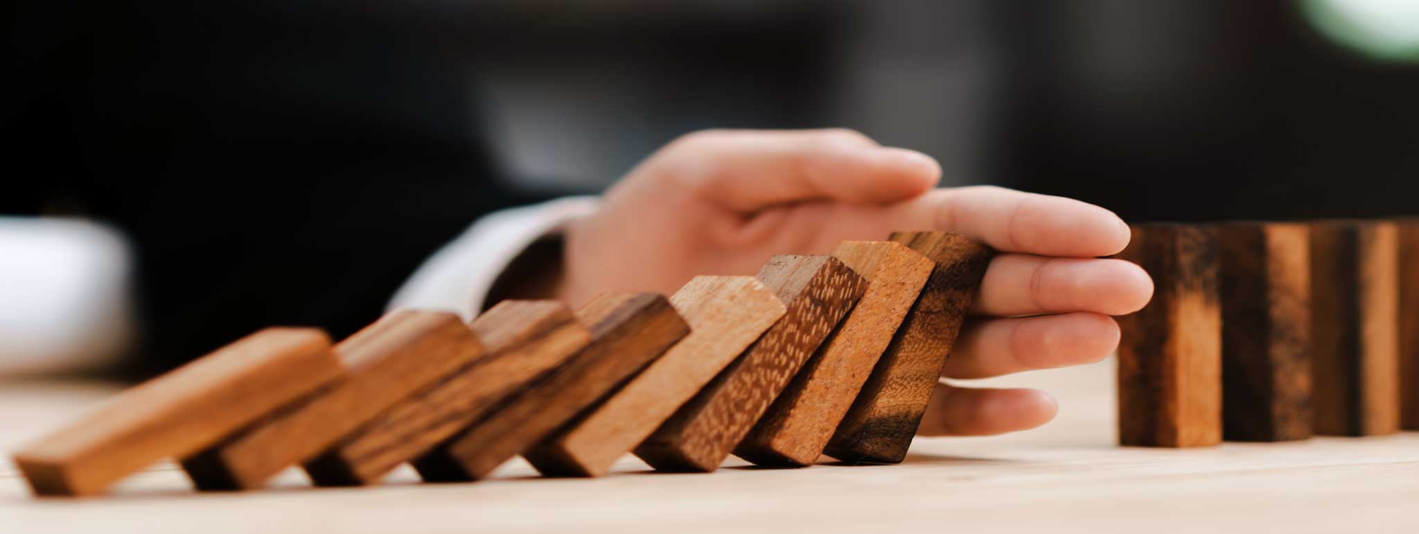 Eine Hand hält fallende Dominosteine auf hellem Tisch an, Symbol für Konfliktlösung bei Lkm GmbH Rechtsanwälte München.
