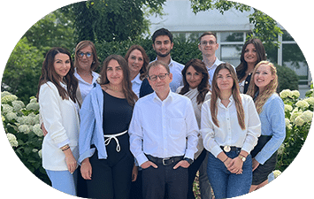 Das Team der Lkm GmbH steht in business-casual Kleidung vor grünen Büschen, weißen Blüten, Bürogebäuden im Hintergrund. Steuerberatung.